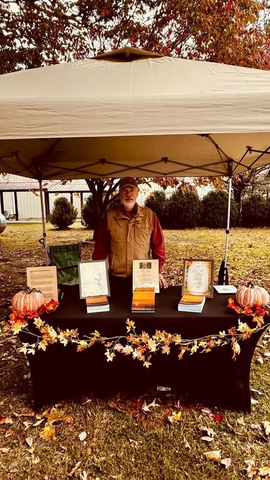 D. E. Johnston at his book table under an autumn canopy